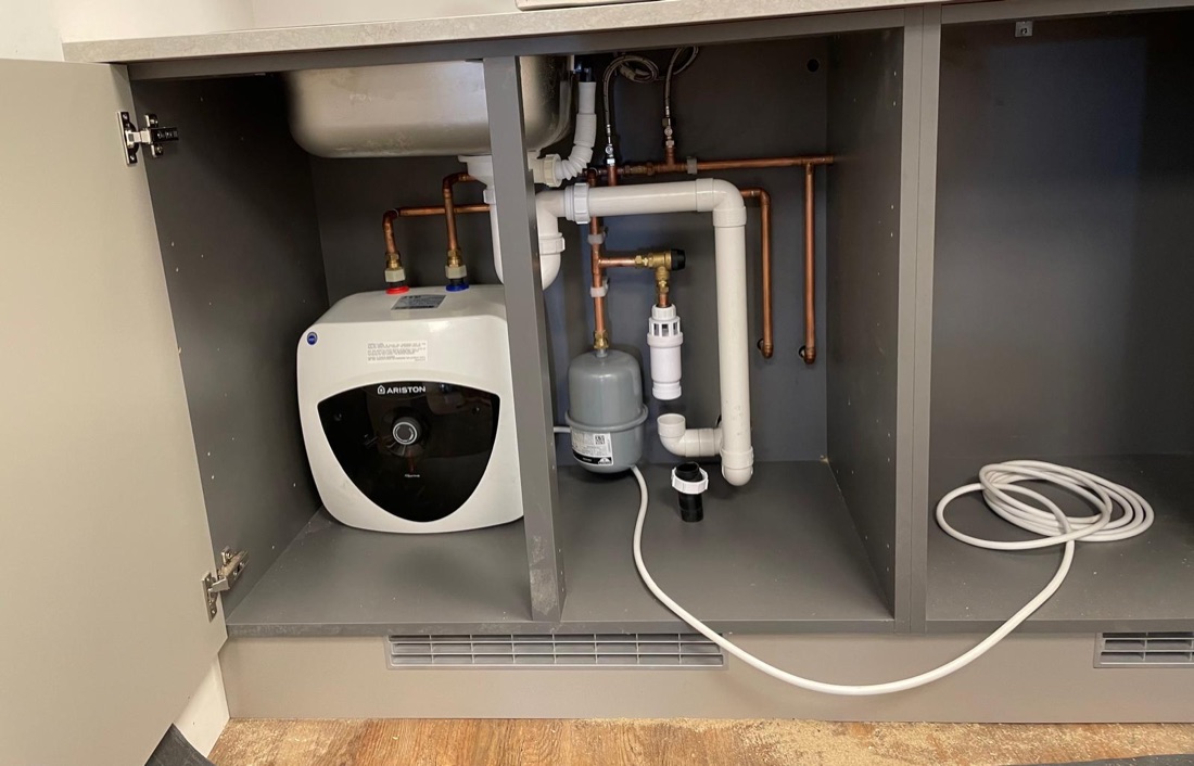 Under-sink water heater with tidy pipework inside a kitchen cupboard